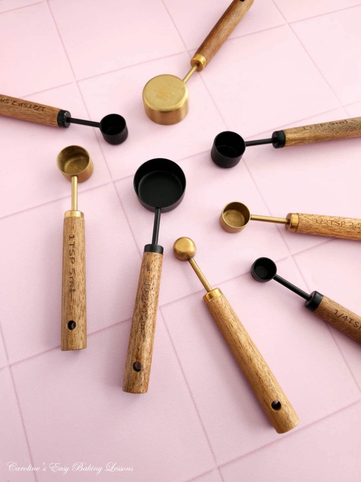 Overhead shot of a pink table with various brass and black wooden handled measuring spoons fanned out.