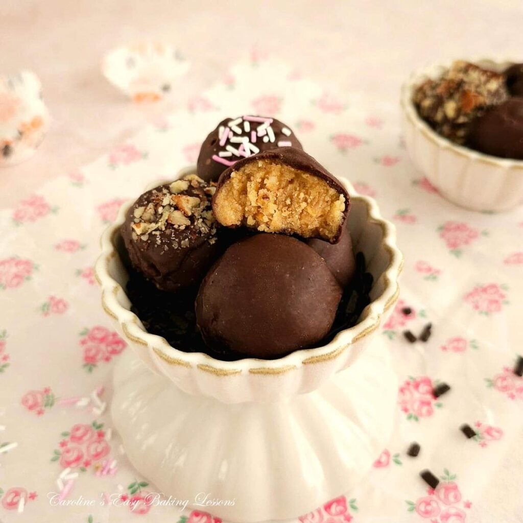 Close shot of small scalloped bowls holding chocolate coated almond truffles, with one showing texture form a bite.