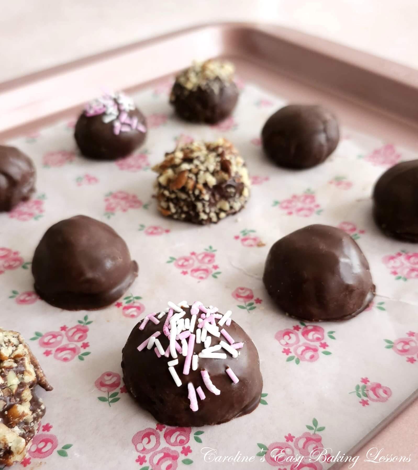 Close diagonal shot of pink/rose gold caookie sheet, paper lined with chocolate coated almond truffles setting.