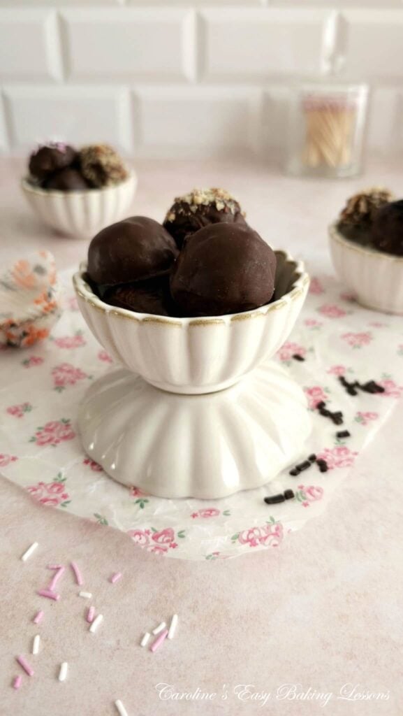 Long shot of a table with bowls of chocolate coated almond truffles, and sprinkles on the table.