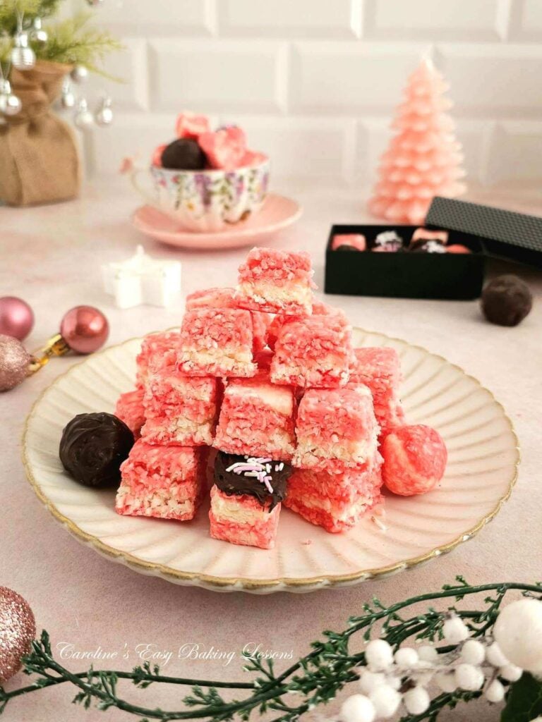 Stack of pink and white marbled coconut ice squares, on beige plate, with Christmas teee and decorations to the back.
