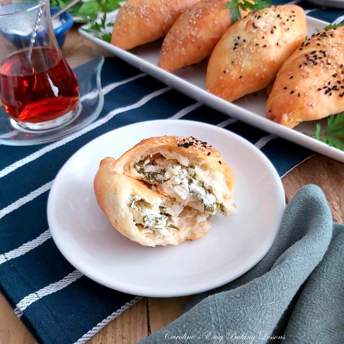 Close shot of a wooden table top with plate of yeast-free pogaca, Turkish cheese stuffed rolls, with one served at the front, showing the filling.