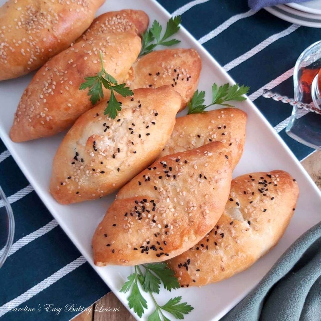 Close overhead shot of white platter with oval shaped cheese stuffed rolls - yeast-free Turkish pogaca.