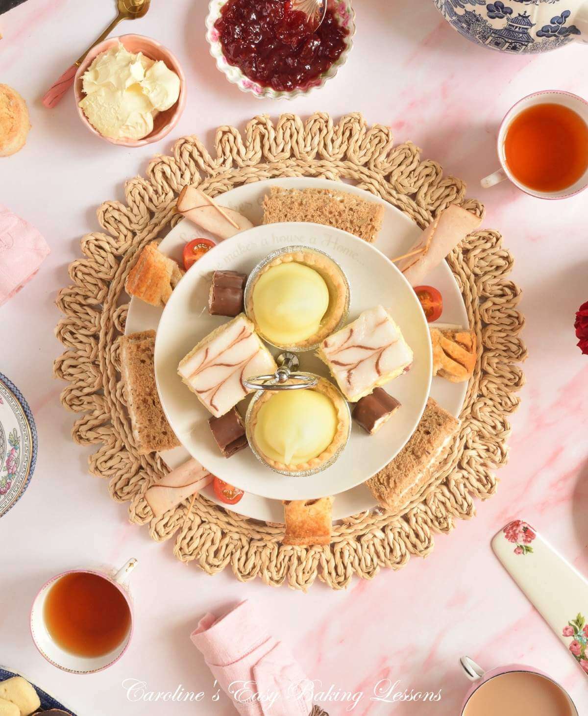 Overheat shot of pink and white marble table with tea party elements, cake stand with savoury nibbles, scones, and hot tea.
