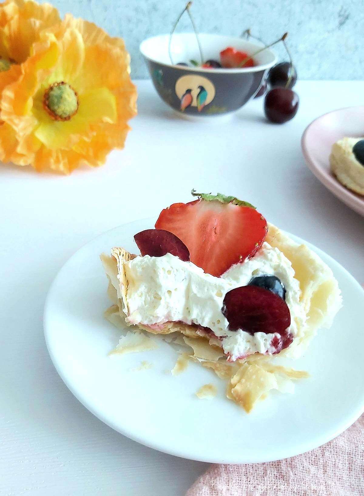 Photo on table, of plate with half eaten puff pastry cup with cream and fresh berries.