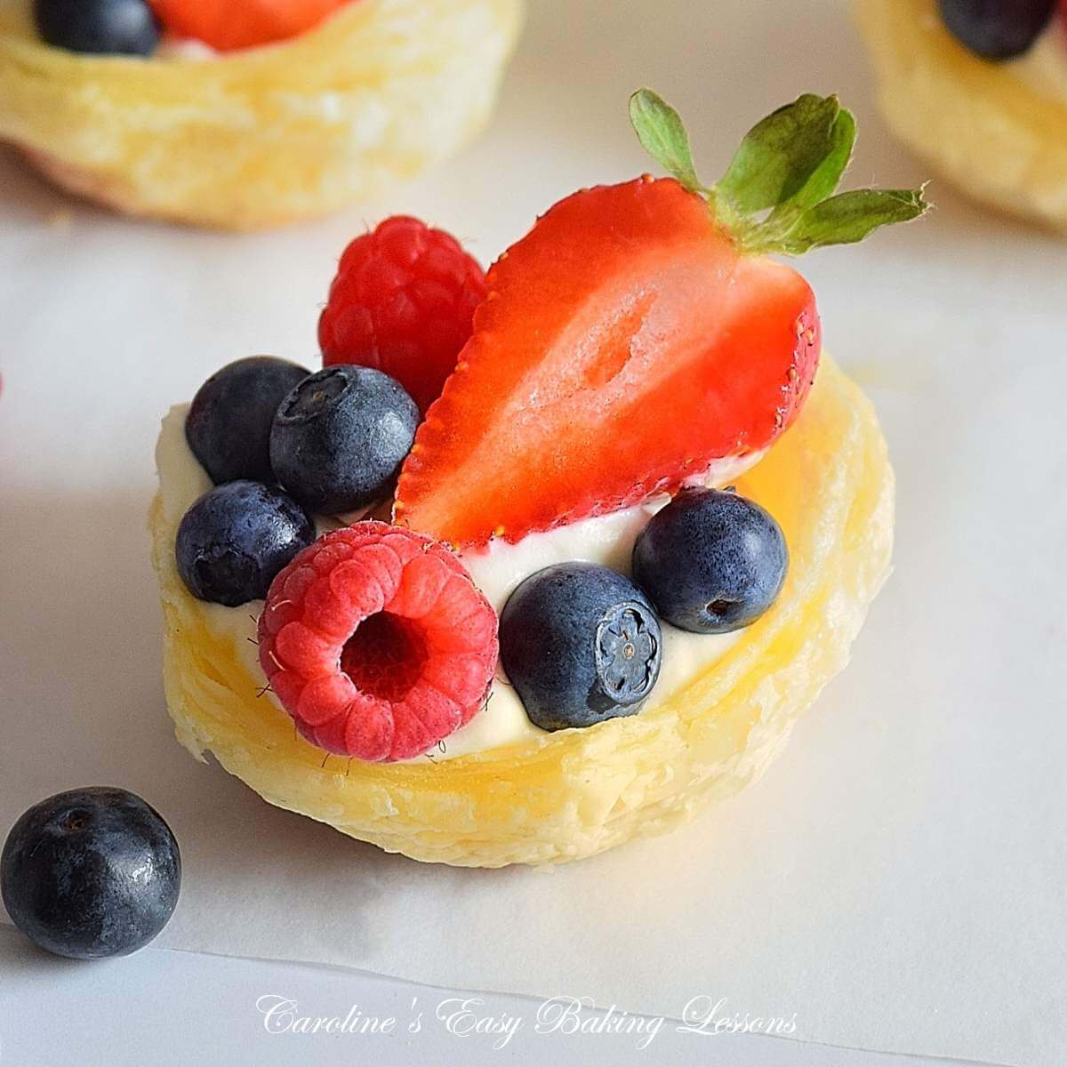 Extra close front on shot of a puff pastry cup, filled with cream, raspberry, blueberries and half strawberry.