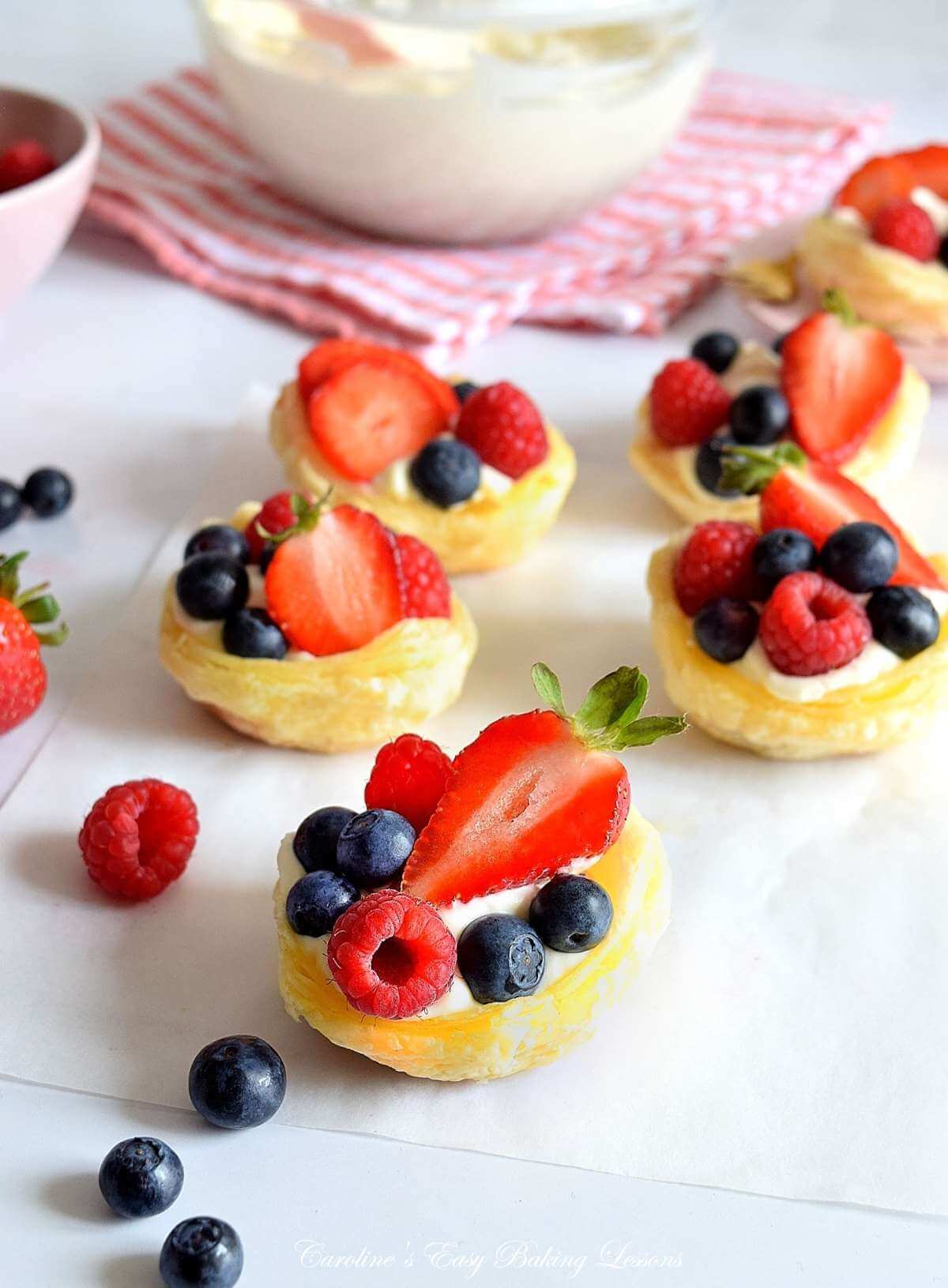 45 degree shot of table top with homemade puff pastry cups, filled with cream and fresh berries and bowl of crema to the background.