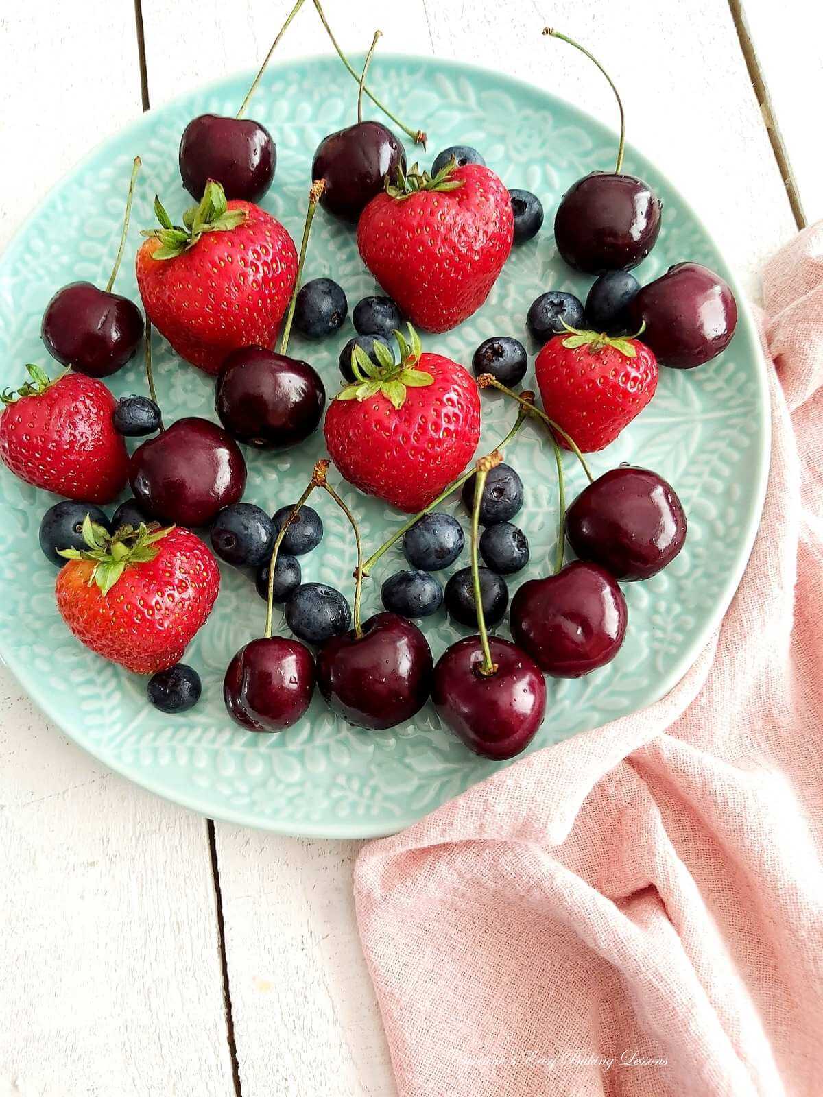 Shot of teal coloured plate, and peach napkin, with fresh strawberries, blueberries and cherries.