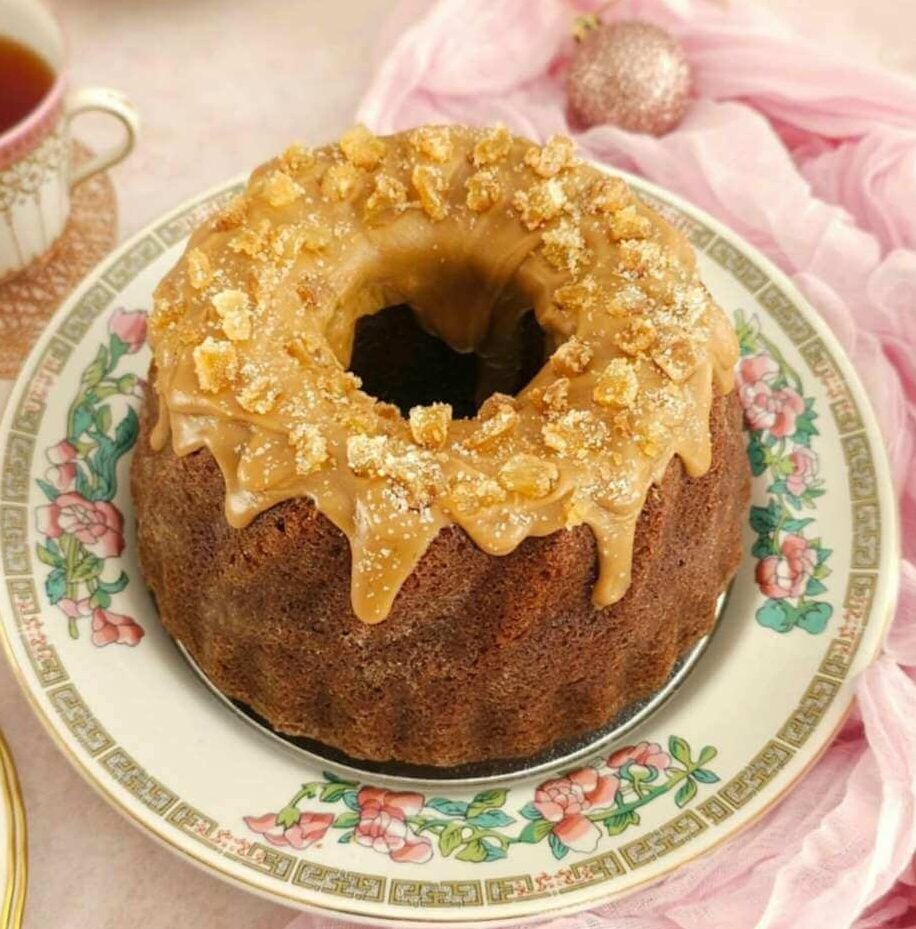 Table with pink and vintage crockery and Cjristmas decorations, surrounding a gingerbread bundt cake with a golden butterscotch glaze and ginger piece son top.