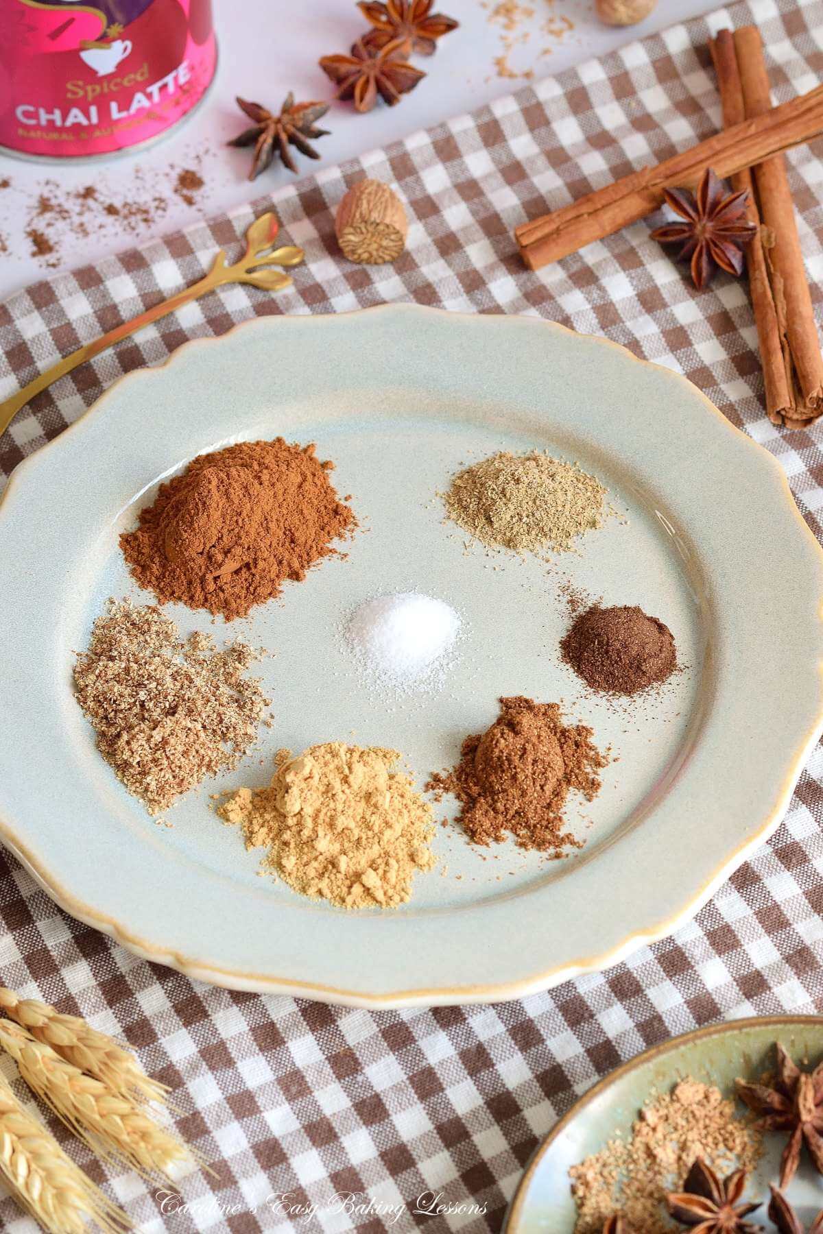 Close angled shot of Autumnal/Fall table with pale green large plate of ground spices for a chai mixture, with chai latte tin, nutmeg, cinnamon and star anise to the sides.