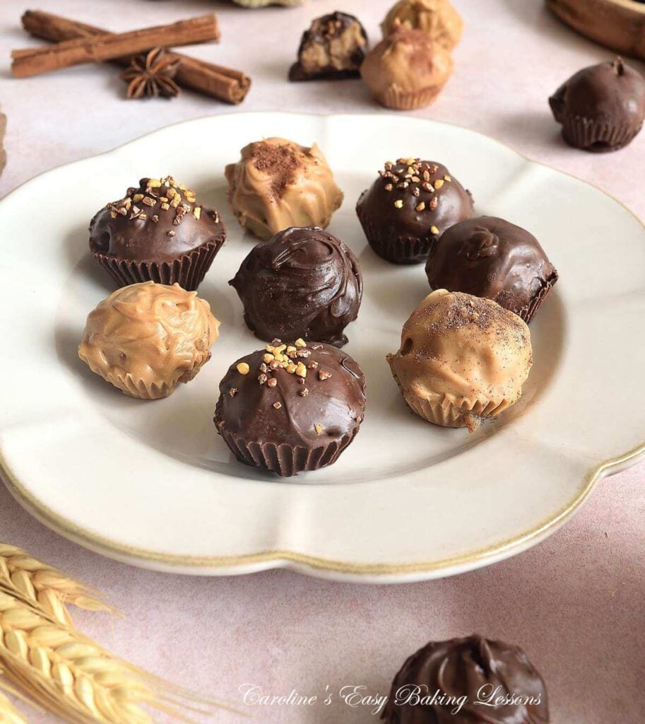 Eye level shot of 8 chocolate coated chai truffles on beige plate with star anise and cinnamon sticks to the background.