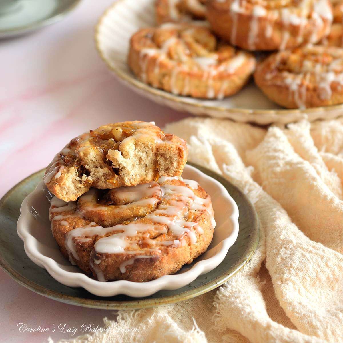 Close eyelevel shot of a quicker pumpkin spice bun, with a bite missing, stacke don top of one plated, wit more to the background.