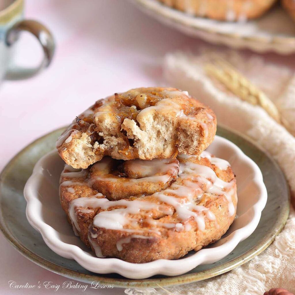 Extra close shot of a quicker pumpkin spice roll, one half-eatten stacked on top of another, on biege & green plate, with more at the corber of background.