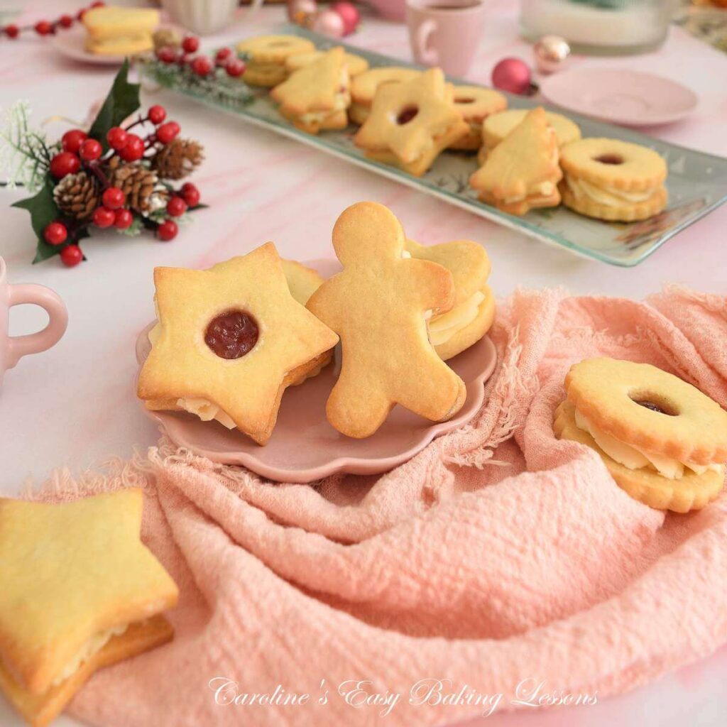 SHot of a pink Christmas table with British Jammie Dodger sandwich cookies in Christmas shapes, gingerbread man and star cookie to the front.