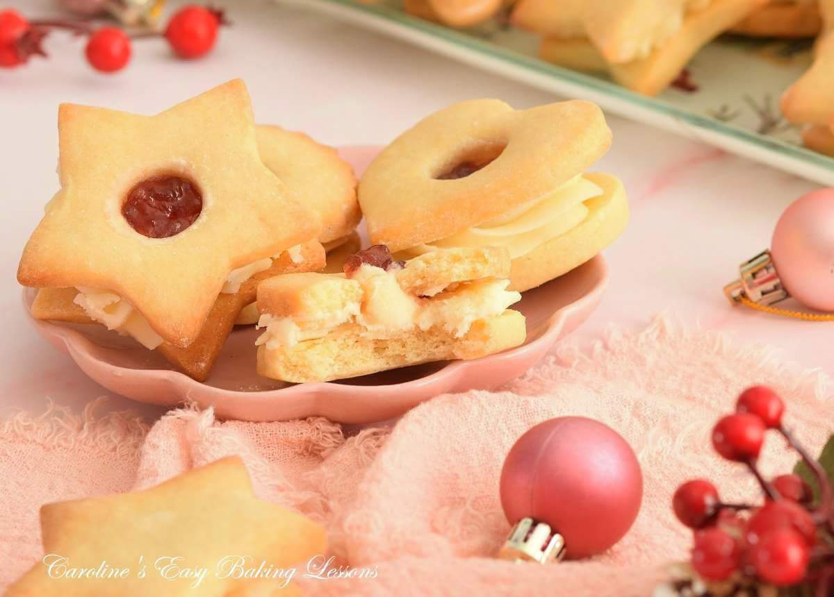 Close shot of pink Christmas table with plate of seasonal Jammie Dodgers, British sandwich cookies, one bitten showing buttercream jam filling.