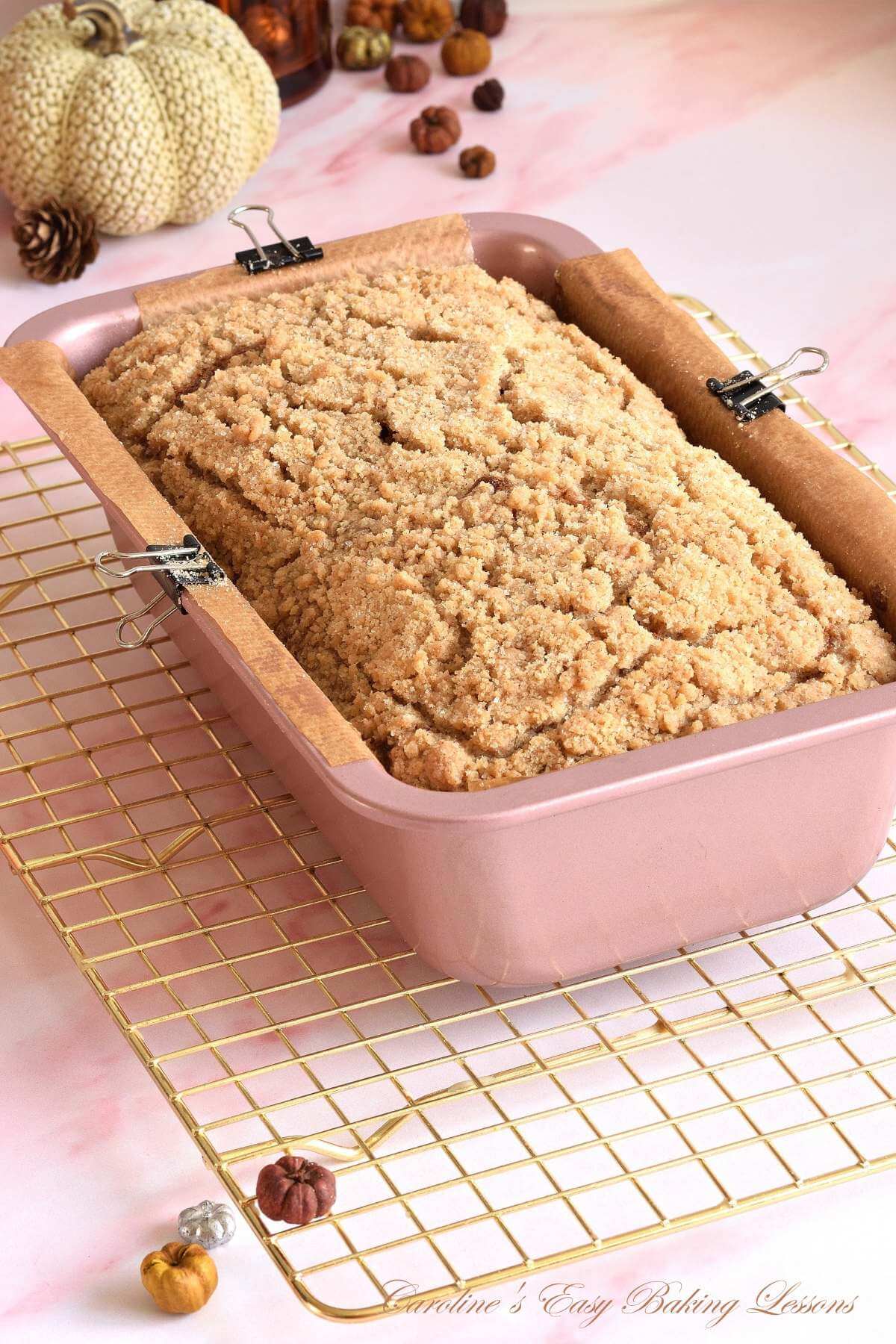 Pink marble wortop/counter with pink/rose gold bread tin with pumpkin streusel bread in it, on ocooling rack.