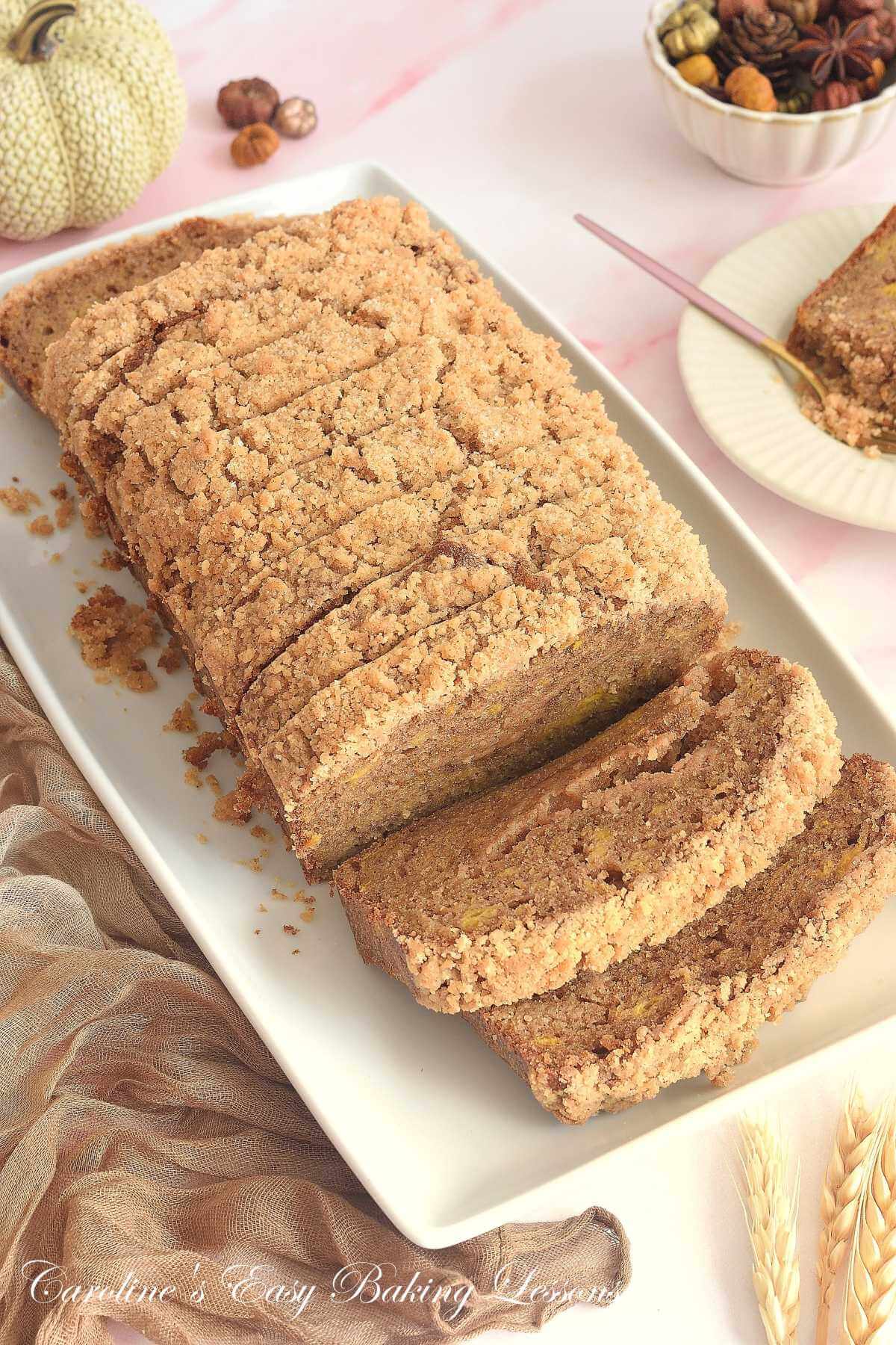 Overhead shot of pumpkin streusel bread, with 11 slices, and one on a plate half-eatten, in an Autumnal setting.