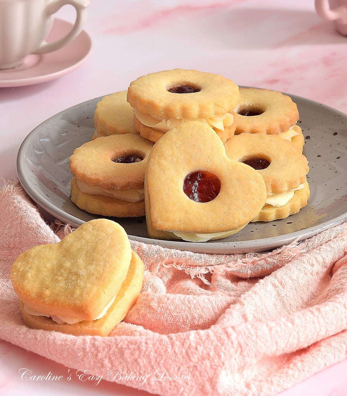 Front 45 degree angled shot of a plate with heart shaped Jammie Dodgers, British buttercream and jam filled sandwich cookies, with pink napkin & crockery.