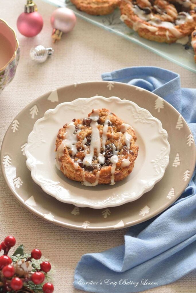 Christmas plate with glazed mince meat swirl bun, with tree baubbles to the background.
