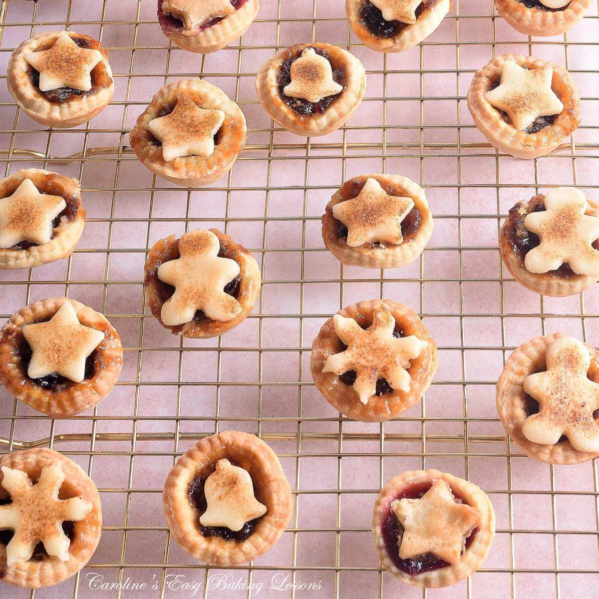 ANgled shot of rose gold cooling rack with golden mini mince pies with seaosnal marzipan toppers cooling.