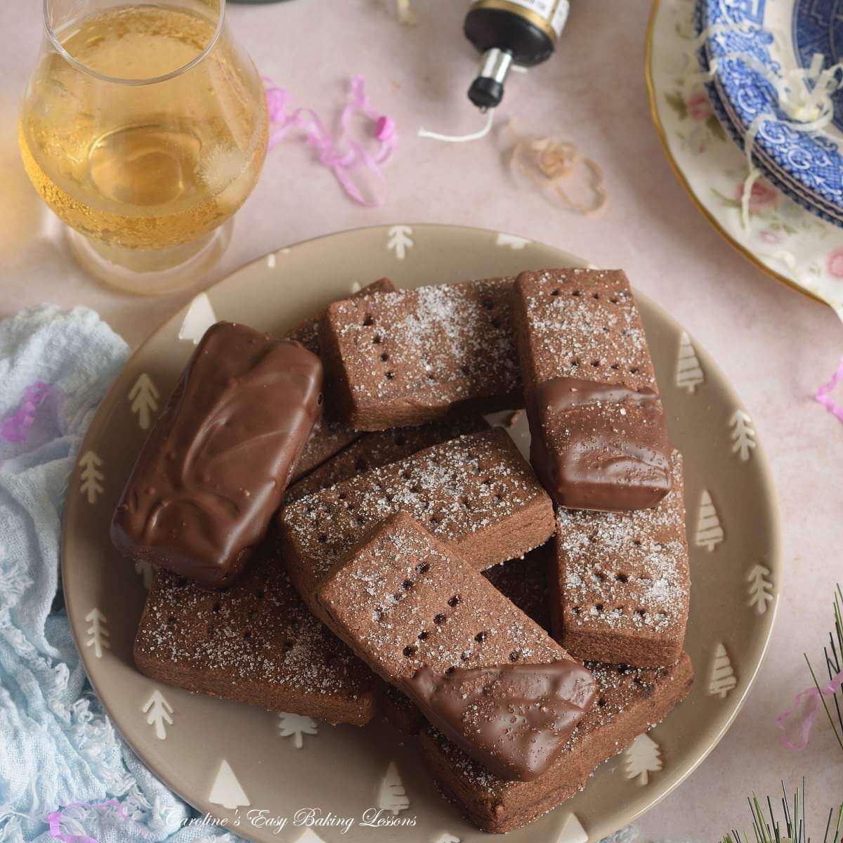 Extra close square shot of a party table with drinks and party poppers, with plate of chocolate & half coated Scottish shortbread.