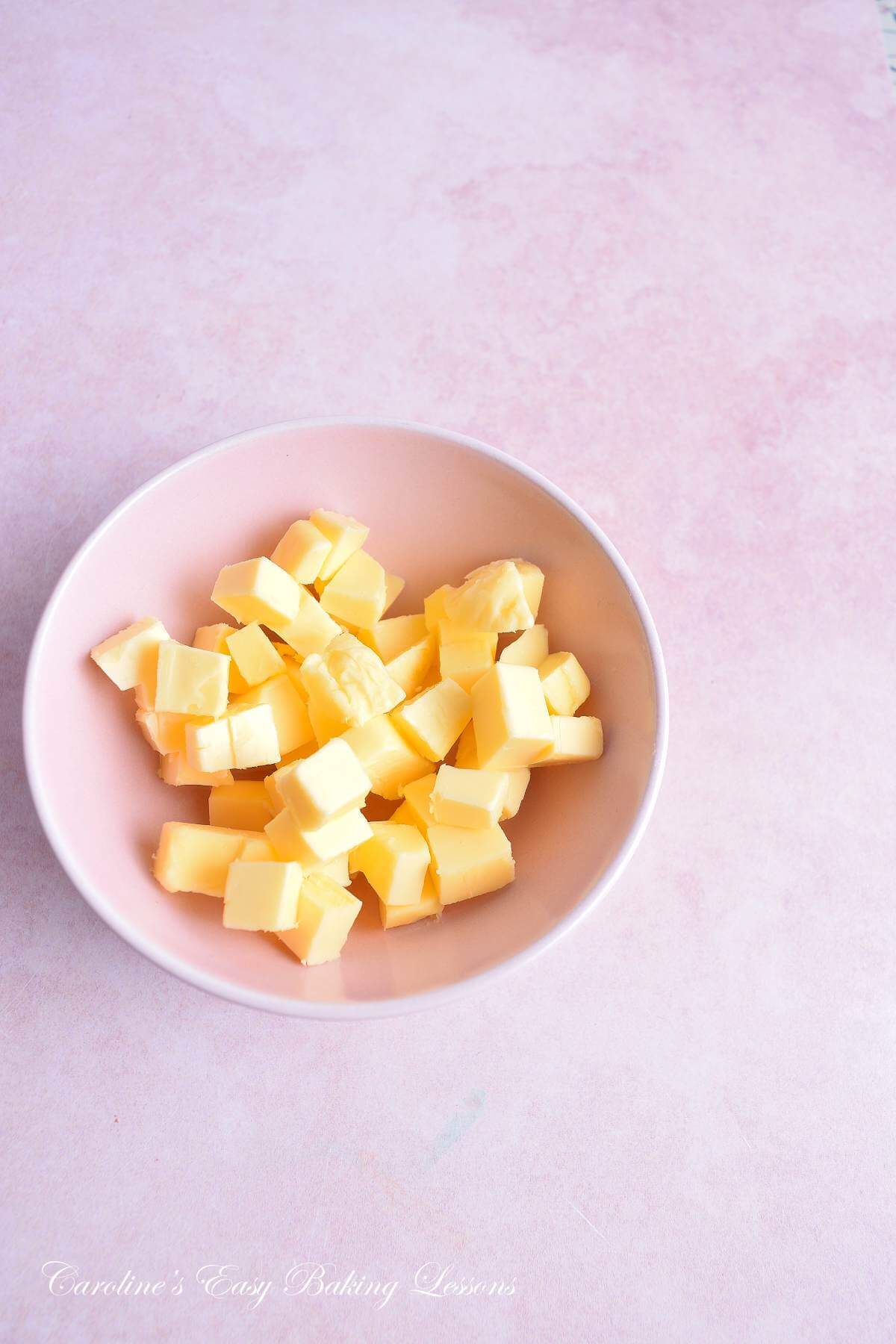 Small pink bowl with small butter cubes, on a pink background.