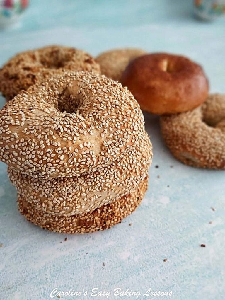 Stack of 3 hoemade sesame coated bagels, with some in the backgorund.