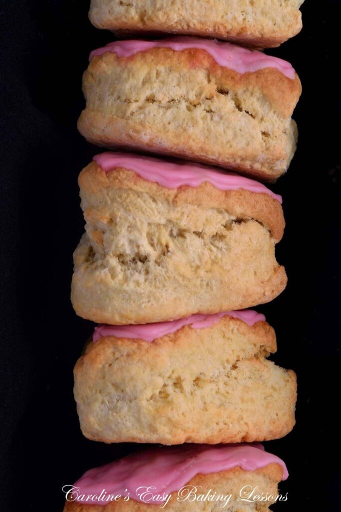 Extra close front on shot of a stack of heart shaped, pink glazed British scones, 5 scones high on black background.