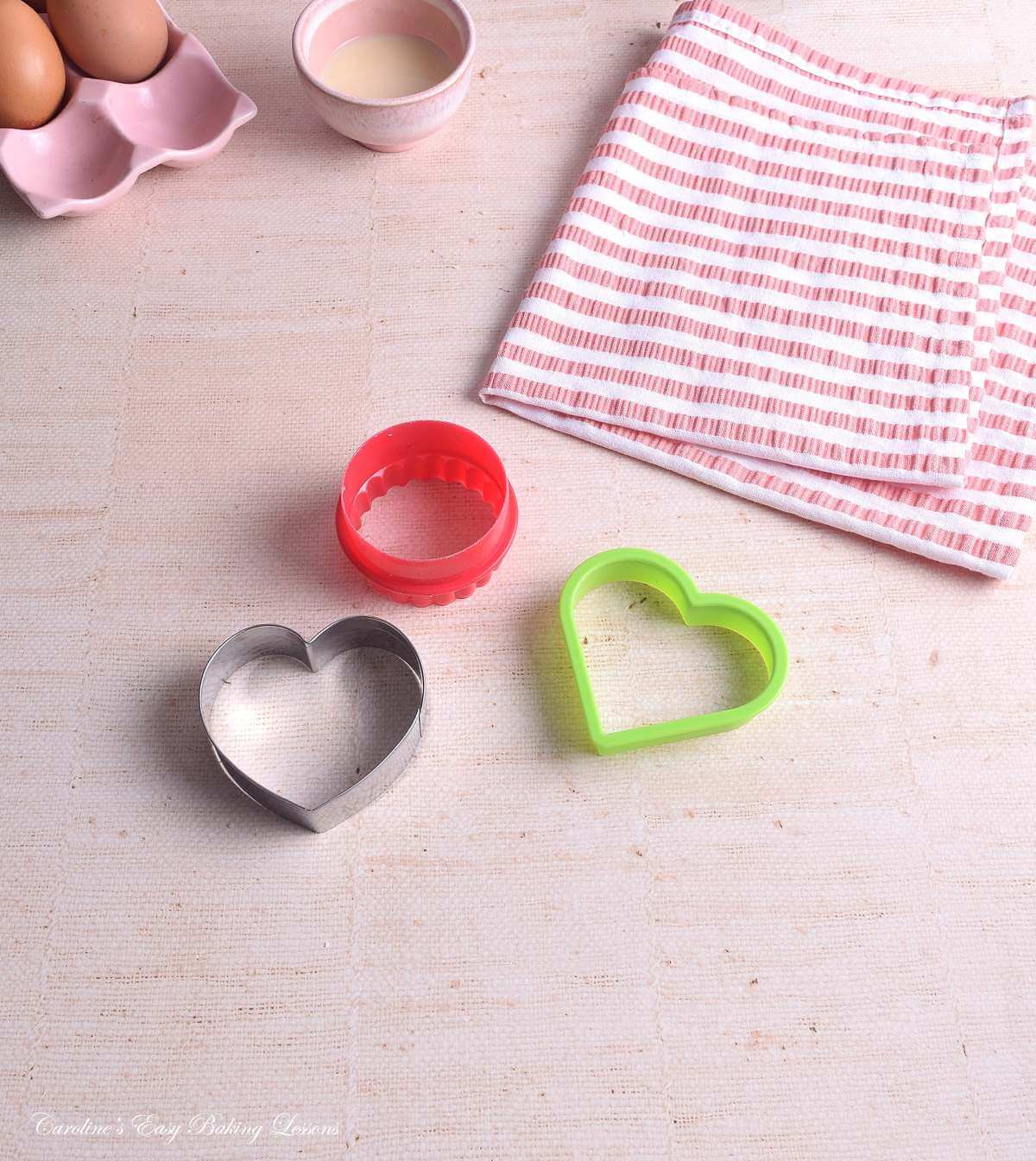 Image on linen table, with red round cookie cutter and 2 larger heart shape cutters.