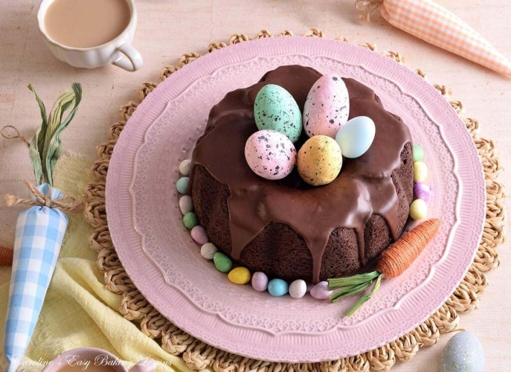 Horizontal image of a pastel Spring table with Easter decorations and devil's Food chocolate bundt cake with large faux Easter eggs inside.
