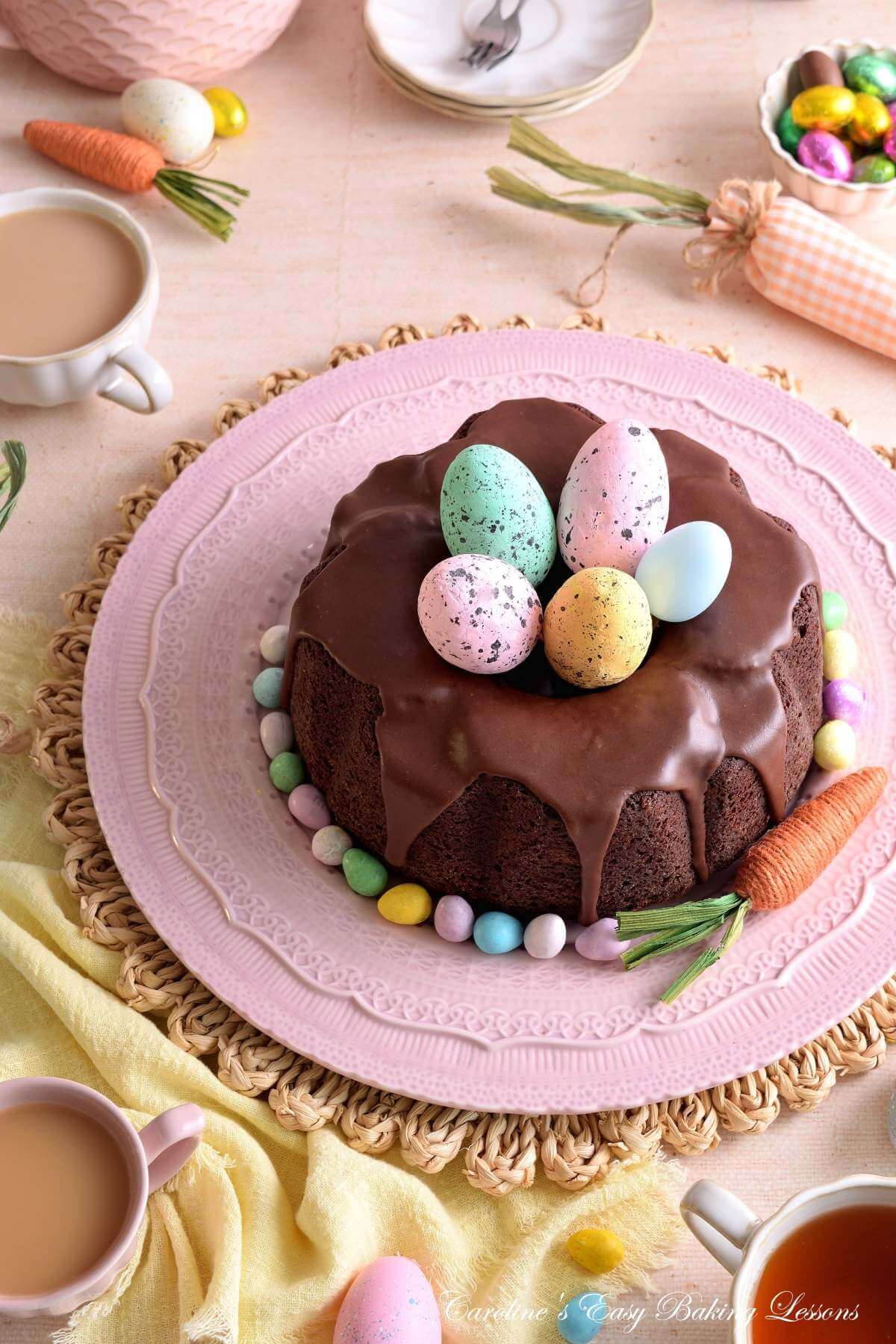 Pastel coloured Easter decorated table with crockery and linen around a Devil's Food chocolate bundt cake, with large faux Easter eggs in the centre.