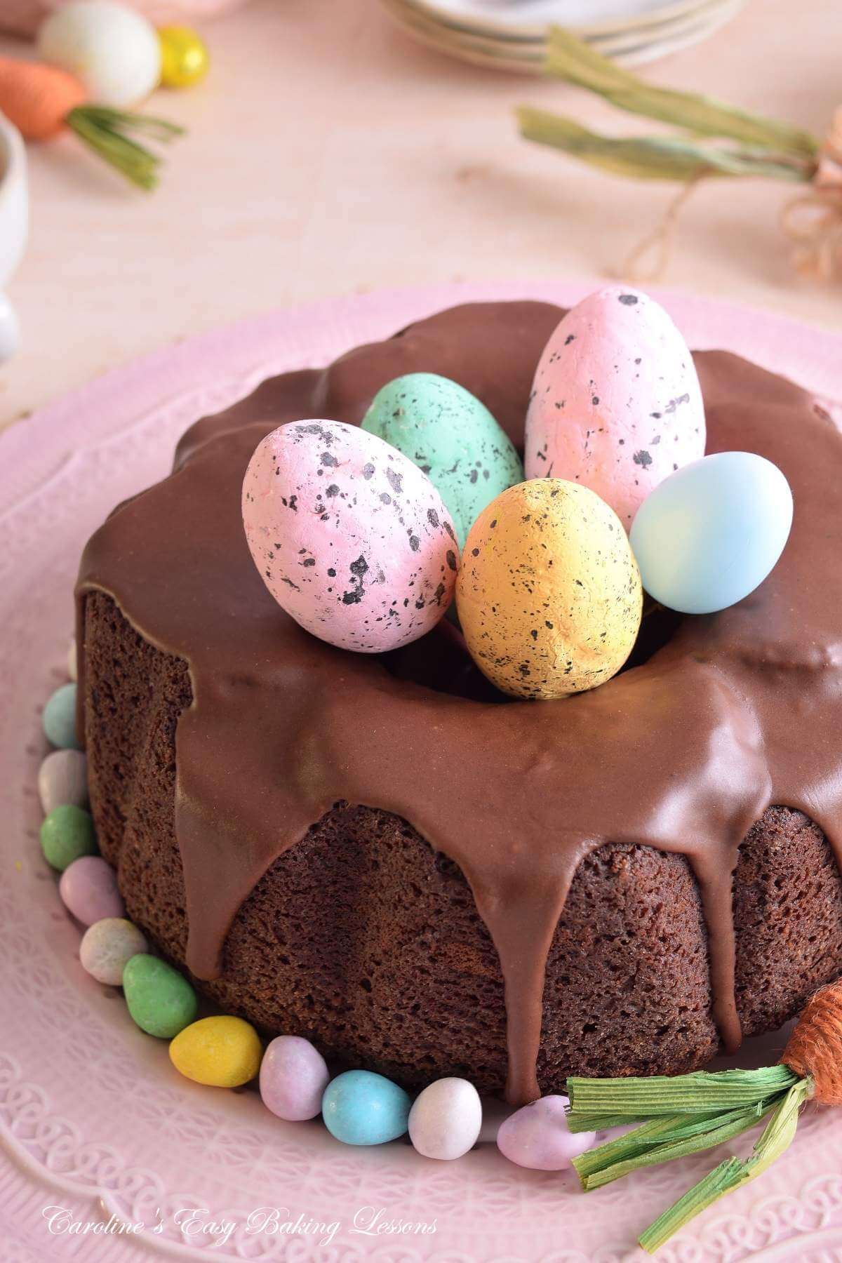Close, partial verticla shot of a Devil's Food chocolate bundt cake with large faux Easter eggs and pastel crockery.