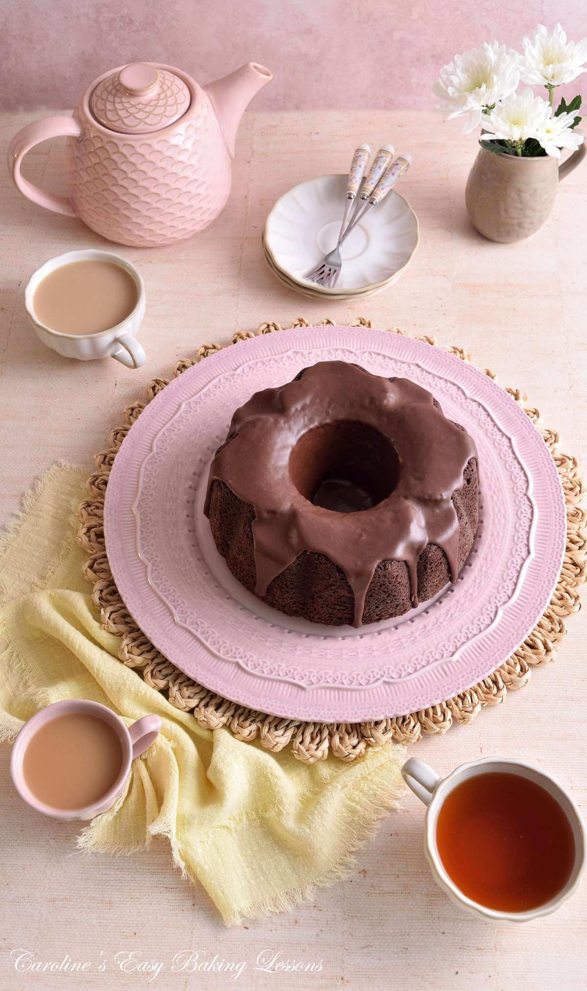 Flat lay image of a pastel tablle of crockery and linen, with a devil's Food chocolate bundt cake in the centre with chocolate glaze.