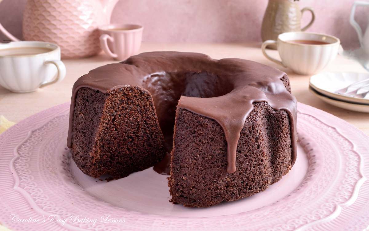 Horizontal image of a pastel pink table with a Devil's Food chocolate bundt cake with a slice missing.