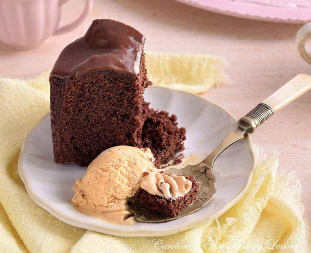 Horizontal image of a pastel table with a close shot of a slice of Devil's Food chocolate bundt cake served and started to be eaten with icecream.