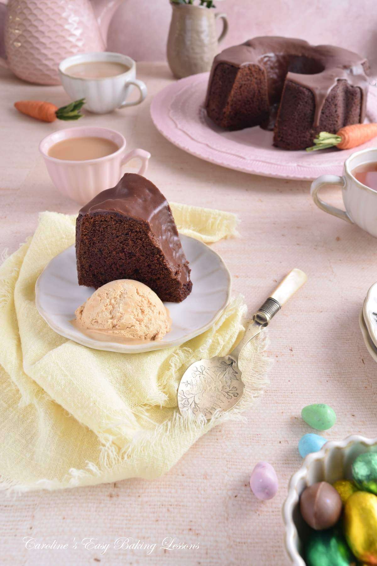Long shot of a pastel Spring coloured table with a tall slice of Devil's Food chocolate bundt cake served with icecream and the rest of the cake to the background.