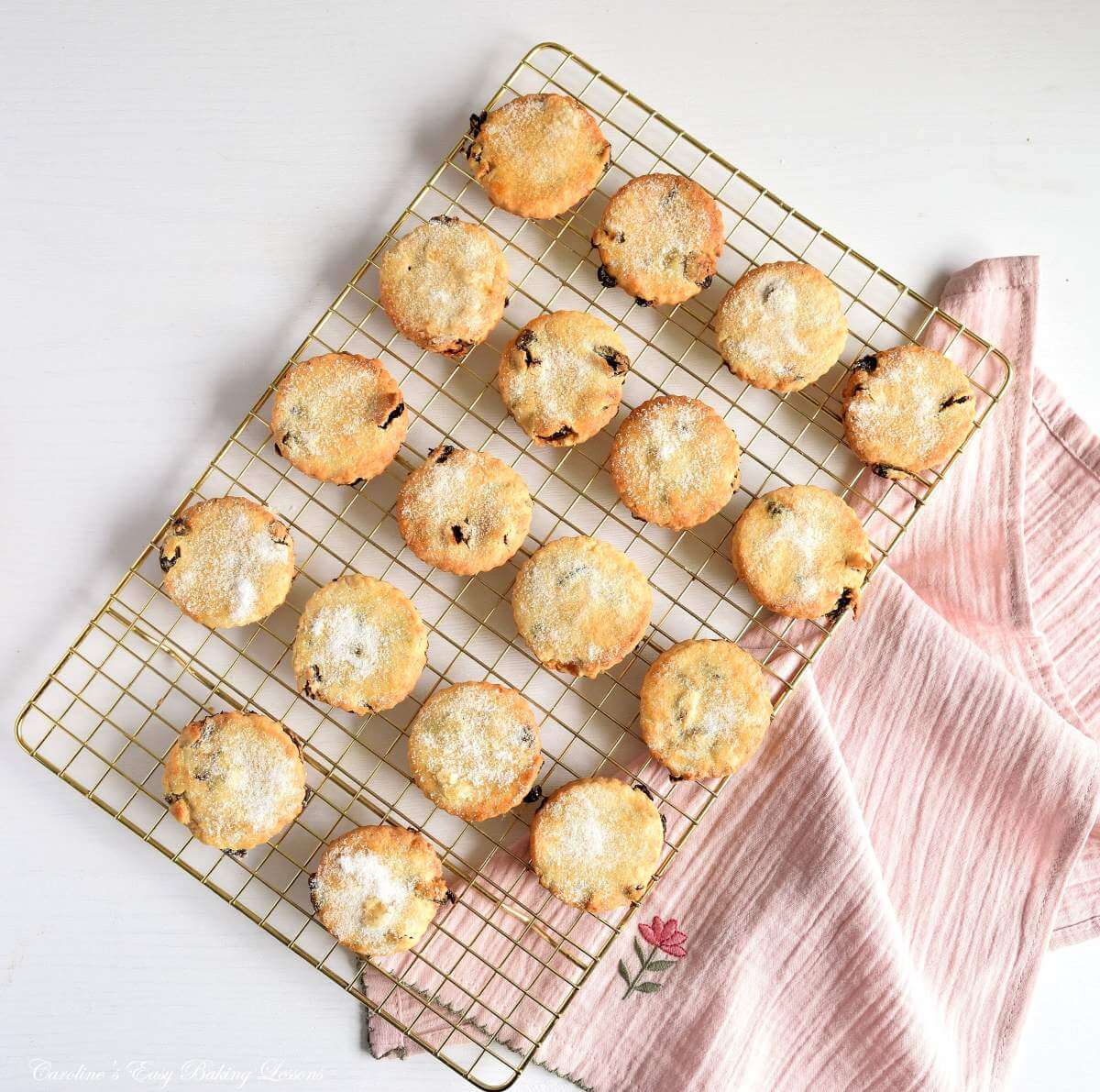 Overhead image of a rose gold cooling rack and pink napkin, with Mary Berry Easter biscuits/cookies cooling.