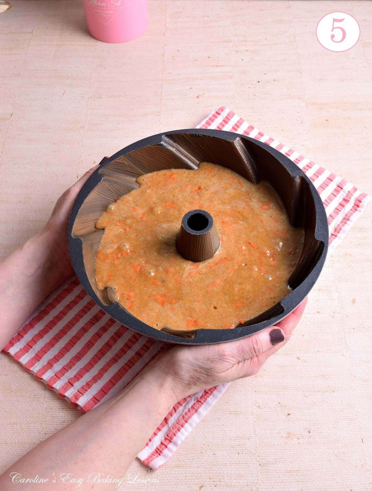 Image of female hands holding a bundt tin filled with gluten-free carrot cake batter ready to bake, with text 'photo 5'.