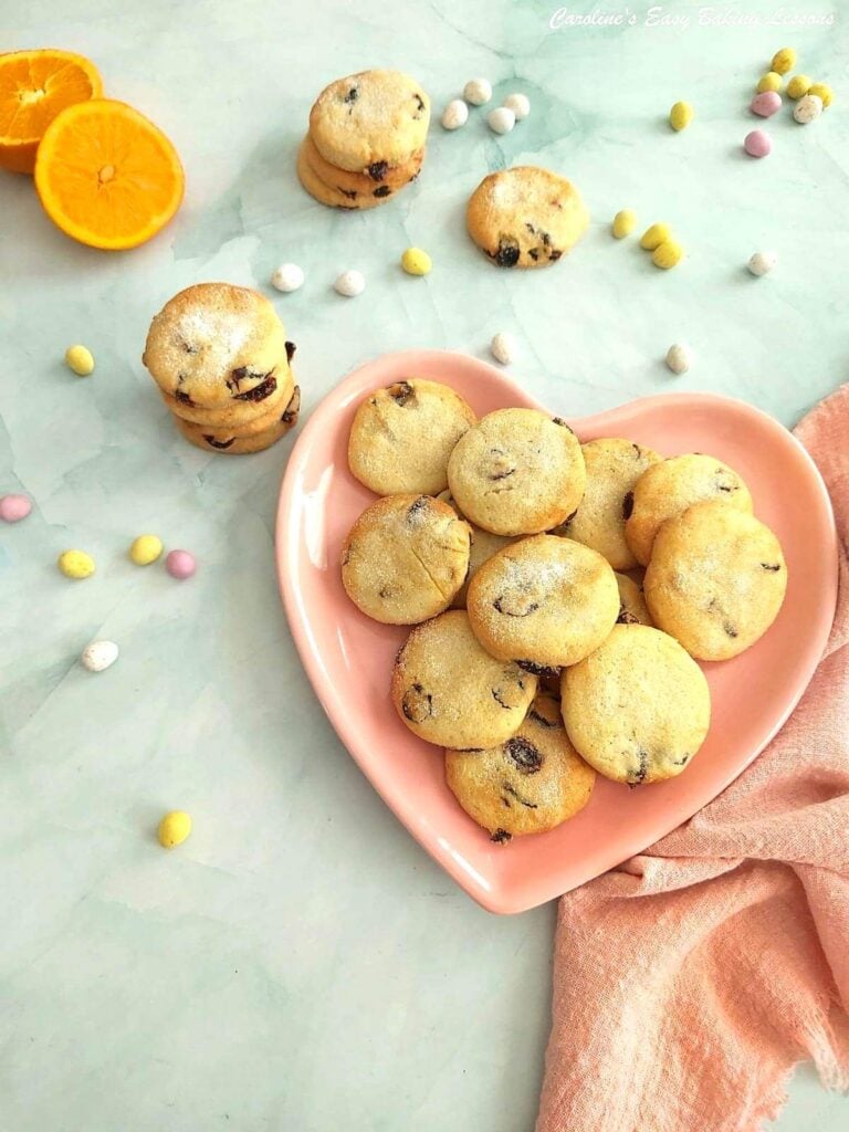 Overhea dimage on pale blue backdrop of cranberry orange Easter Biscuits, some in a stack, some on a pink heart plate and mini chocolate eggs.