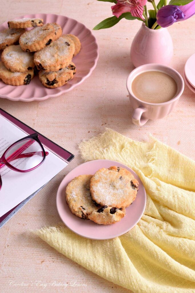 45 degree angeled shot of apstel coloured table with linene and crockery, flower, coffee, book and reading glasses surrounding a plate of Easter biscuits/cookies.