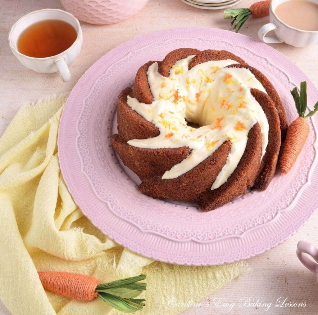 Overhead anged image of Spring table with pastel coloured napkin and props and a large gluten-free carrot bundt cake with cream cheese frosting.