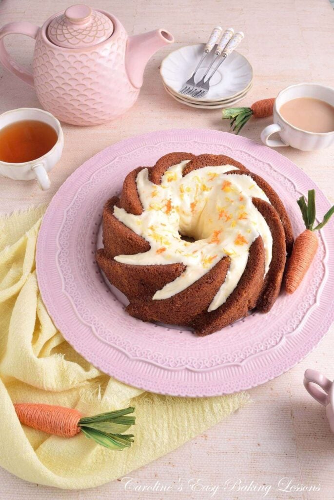 45 degree shot looking down on a pastel coloured, Spring looking table with napkin, crockery and eggs/carrot decorations, surrounding a gluten-free carrot bundt cake.