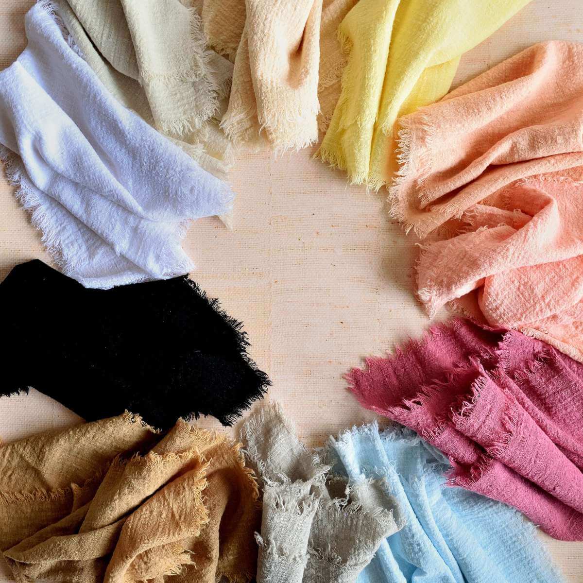 Square overhead image of a circle pattern of various coloured muslin cloth napkins for food photography.
