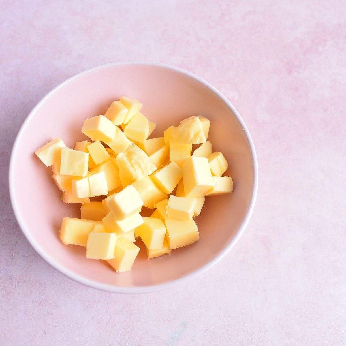 Close overhead shot of pink bowl of small cubed butter pieces on pink background.