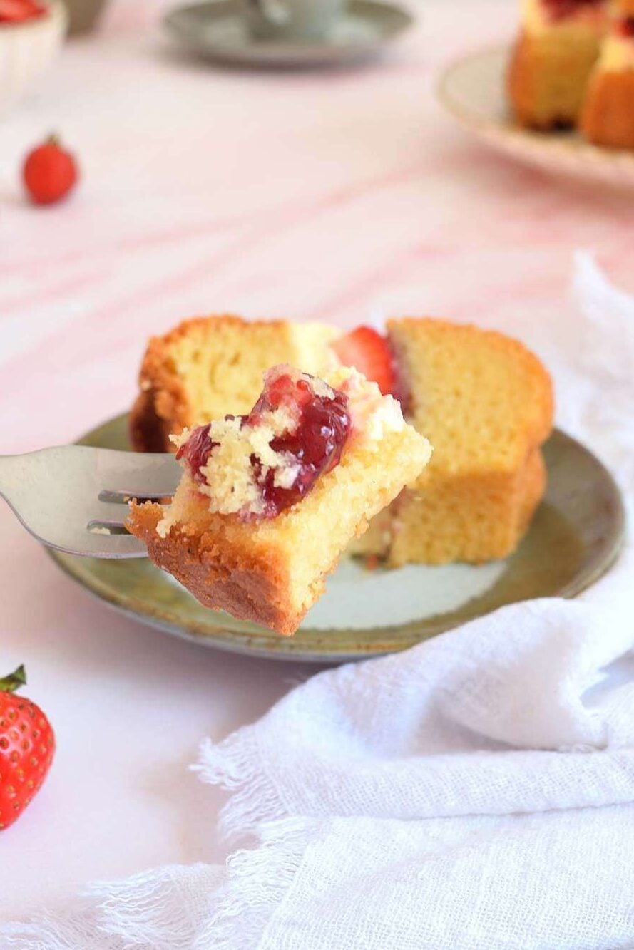 Close shot of a pink marbled table with crockery and flowers, and up close the texture of a piece of Victoria sandwich bundt cake on a fork with the cream jam filling.