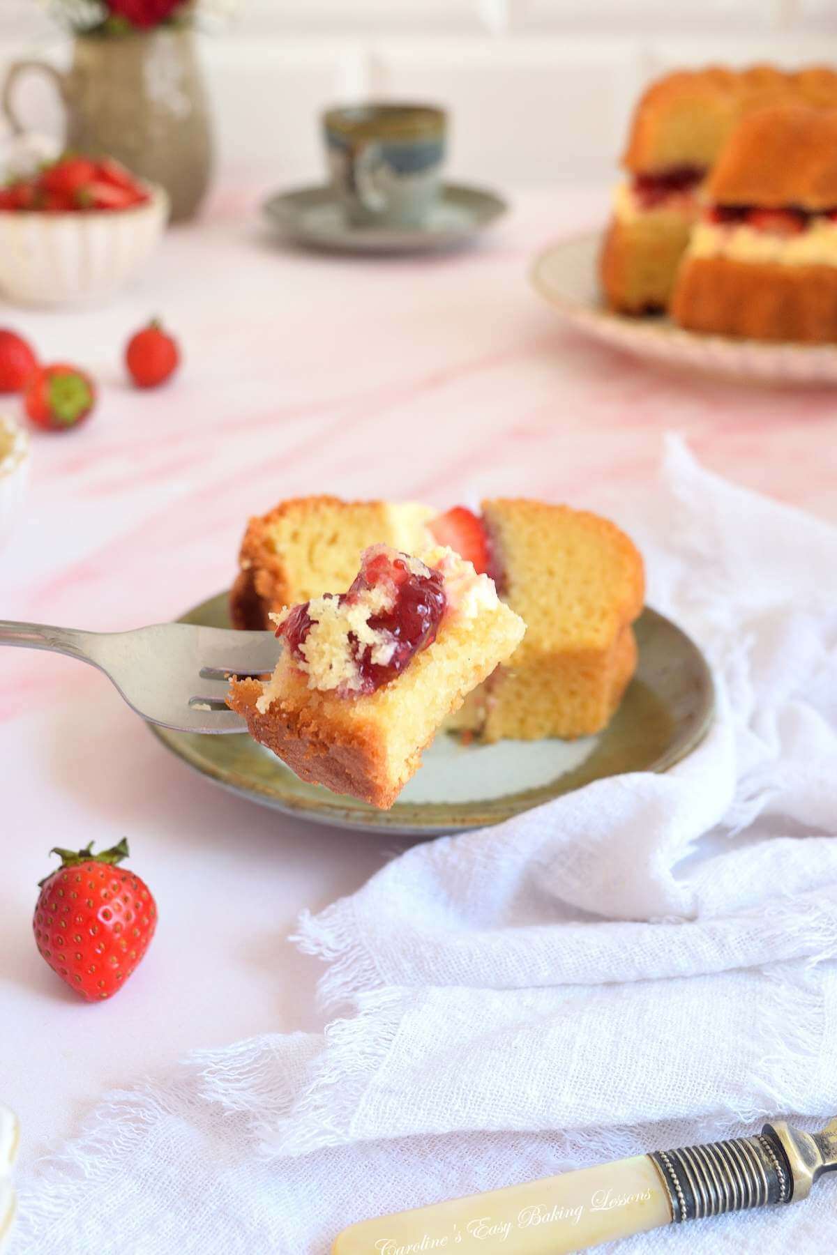 Close shot of a pink marbled table with crockery and flowers, and up close the texture of a piece of Victoria sandwich bundt cake on a fork with the cream jam filling.