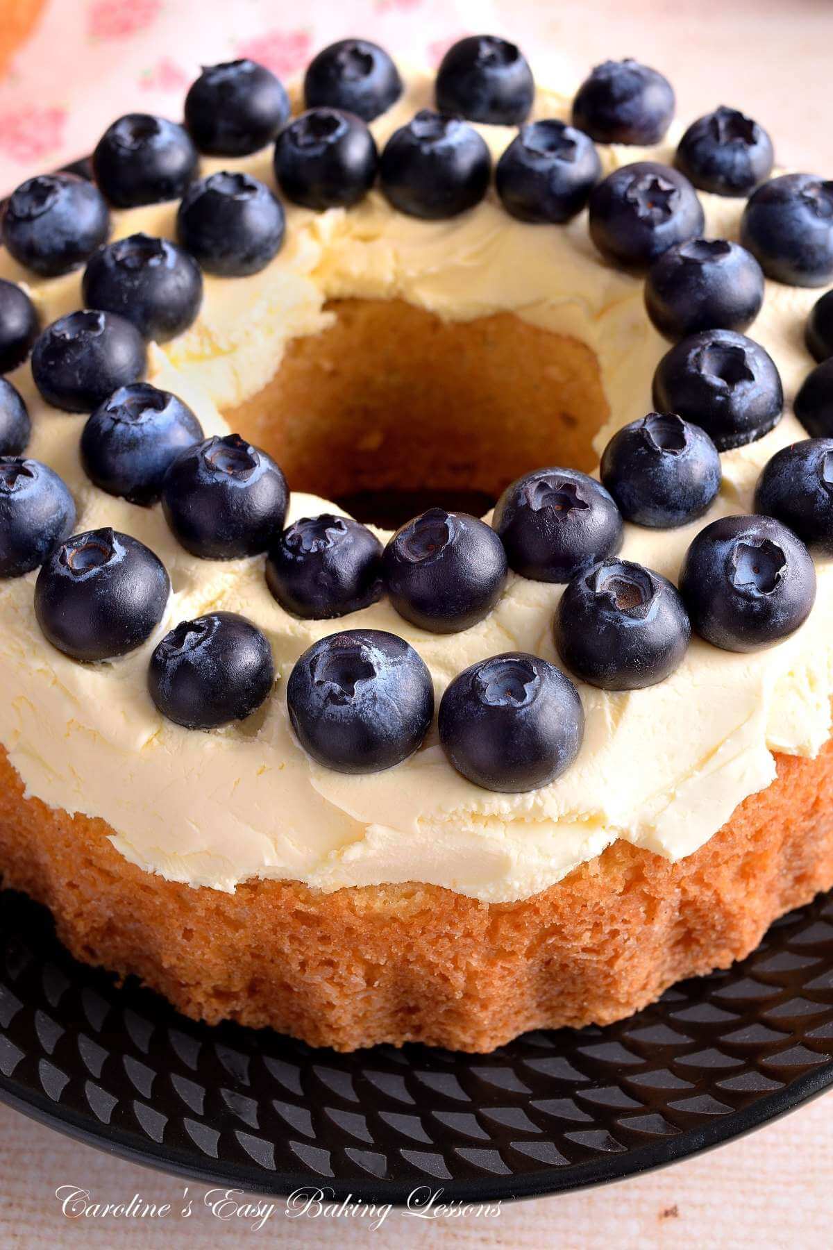 Extra close and partial shot of adding blueberries on top of clotted cream on a layer of bundt cake.