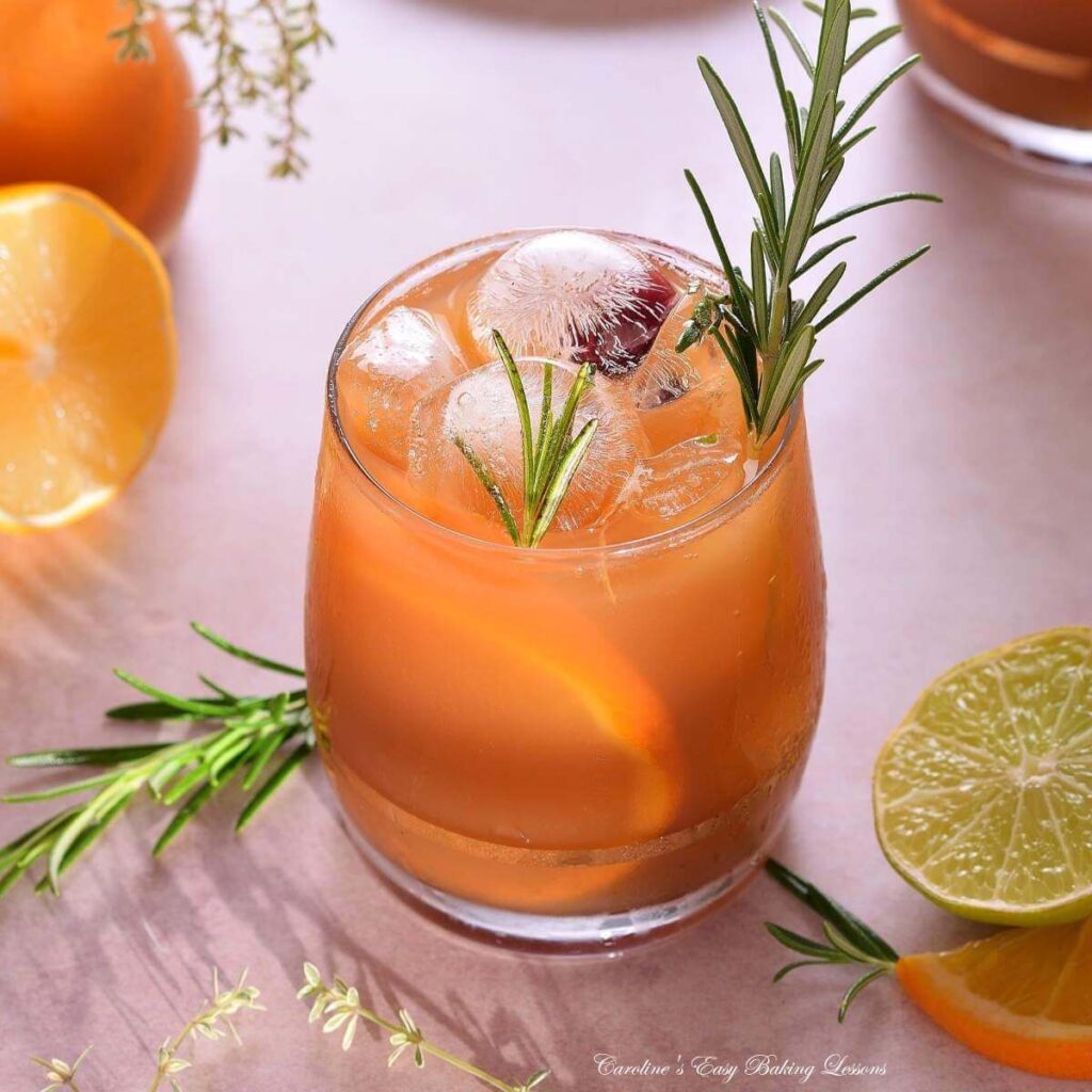 Square image at 45 degrees of a bright citrus iced tea in glass, with lots of ice, rosemary garnish and sunny shadows.