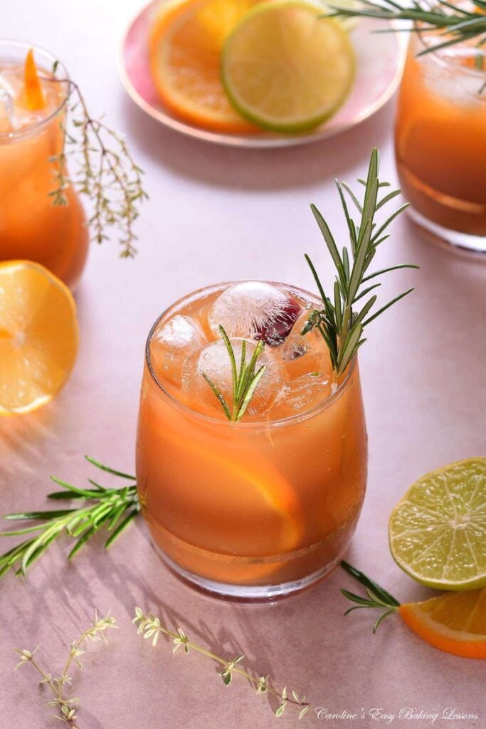 Vertical shot at 45 degrees of a bright citrus iced tea in glass, with lots of ice, rosemary garnish and sunny shadows.