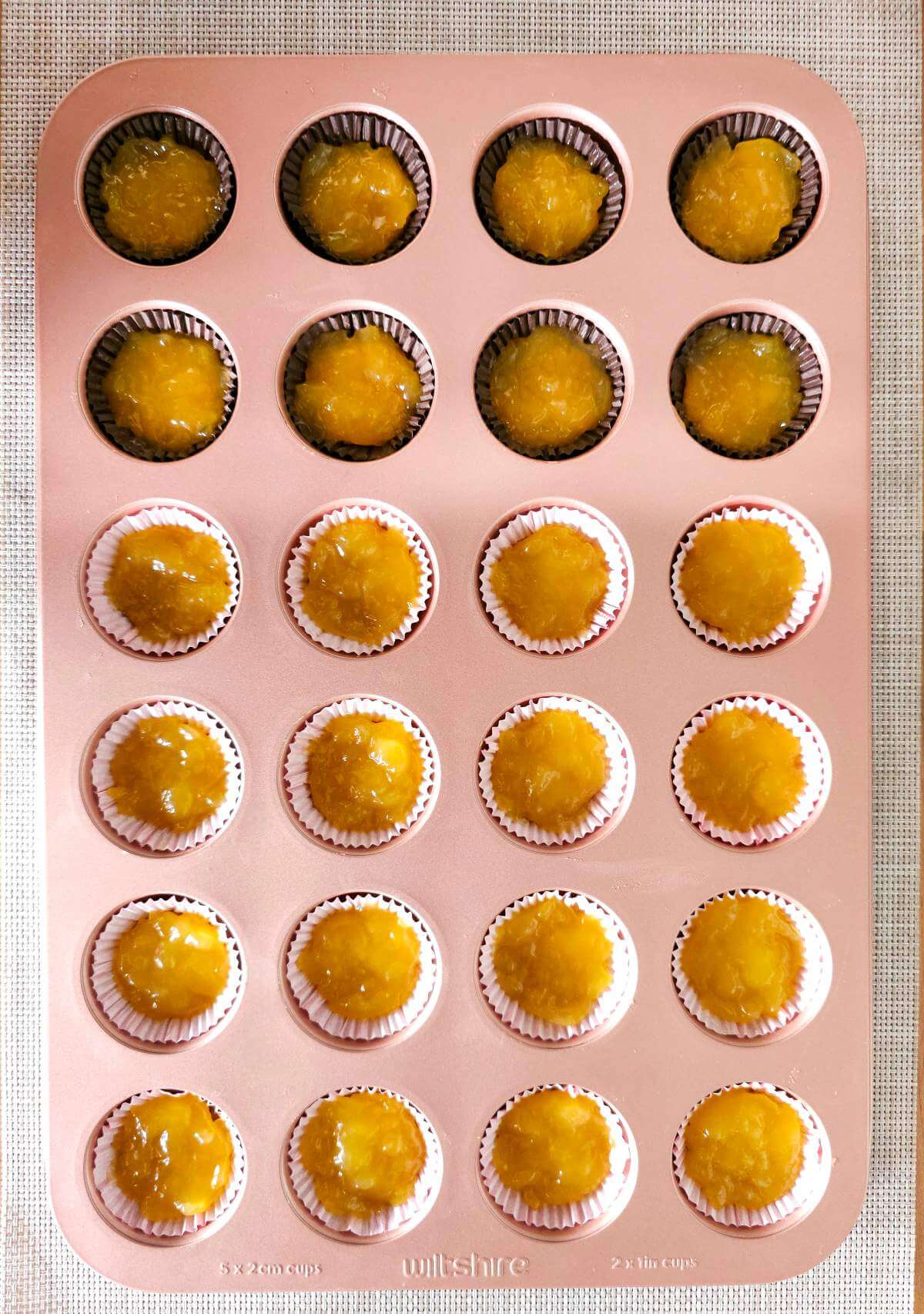Overhead image of pink rose gold Wilton 24-hole mini muffin tin with paper liners and lemon curd layer.